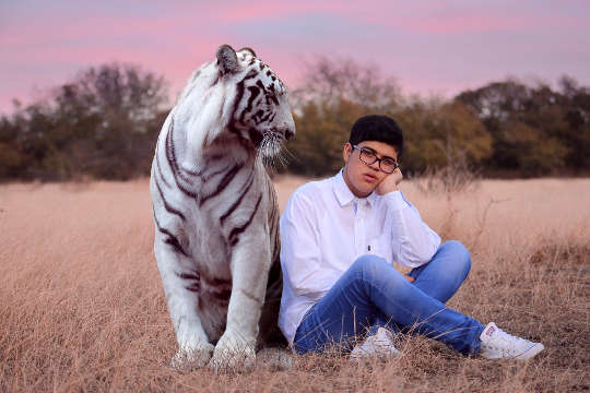 How to Develop Symbolic Communication with Animals young man sitting in a field with a big tiger sitting next to him